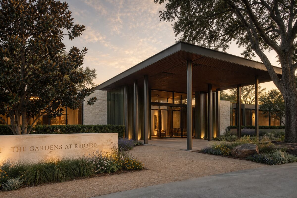 Concept rendering of the front entrance of The Gardens at RedBird at dusk: a covered portico with slender columns, warm light through floor-to-ceiling glass, and a carved limestone monument sign reading The Gardens at RedBird.