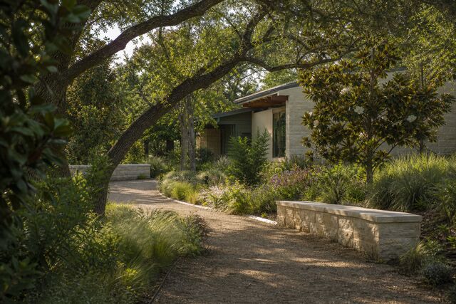 Concept rendering of a shaded garden walking path bordered by native Texas grasses and magnolia trees, leading toward a low limestone care building.